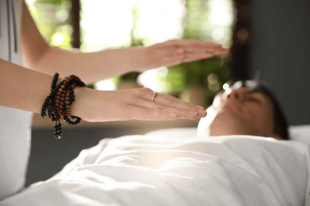 A practitioner performing energy healing with hands hovering above a relaxed individual lying on a table, surrounded by soft lighting and greenery.