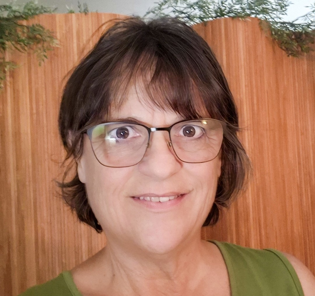 Portrait of Sharon wearing glasses and a green top outdoors.